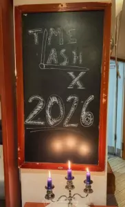Kreidetafel mit der Aufschrift TimeLash X 2026 und drei brennenden violetten Kerzen